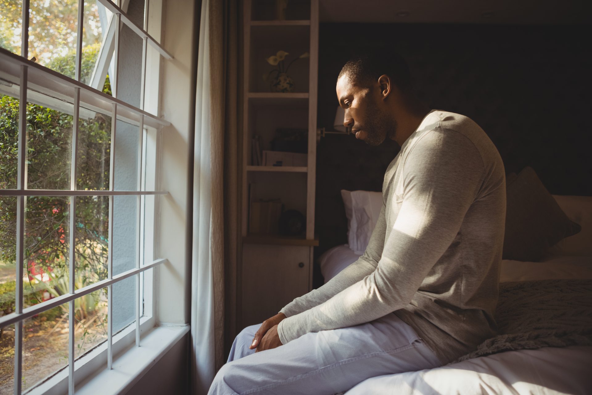 side-view-of-sad-man-sitting-on-bed-by-window-2022-02-02-03-59-18-utc
