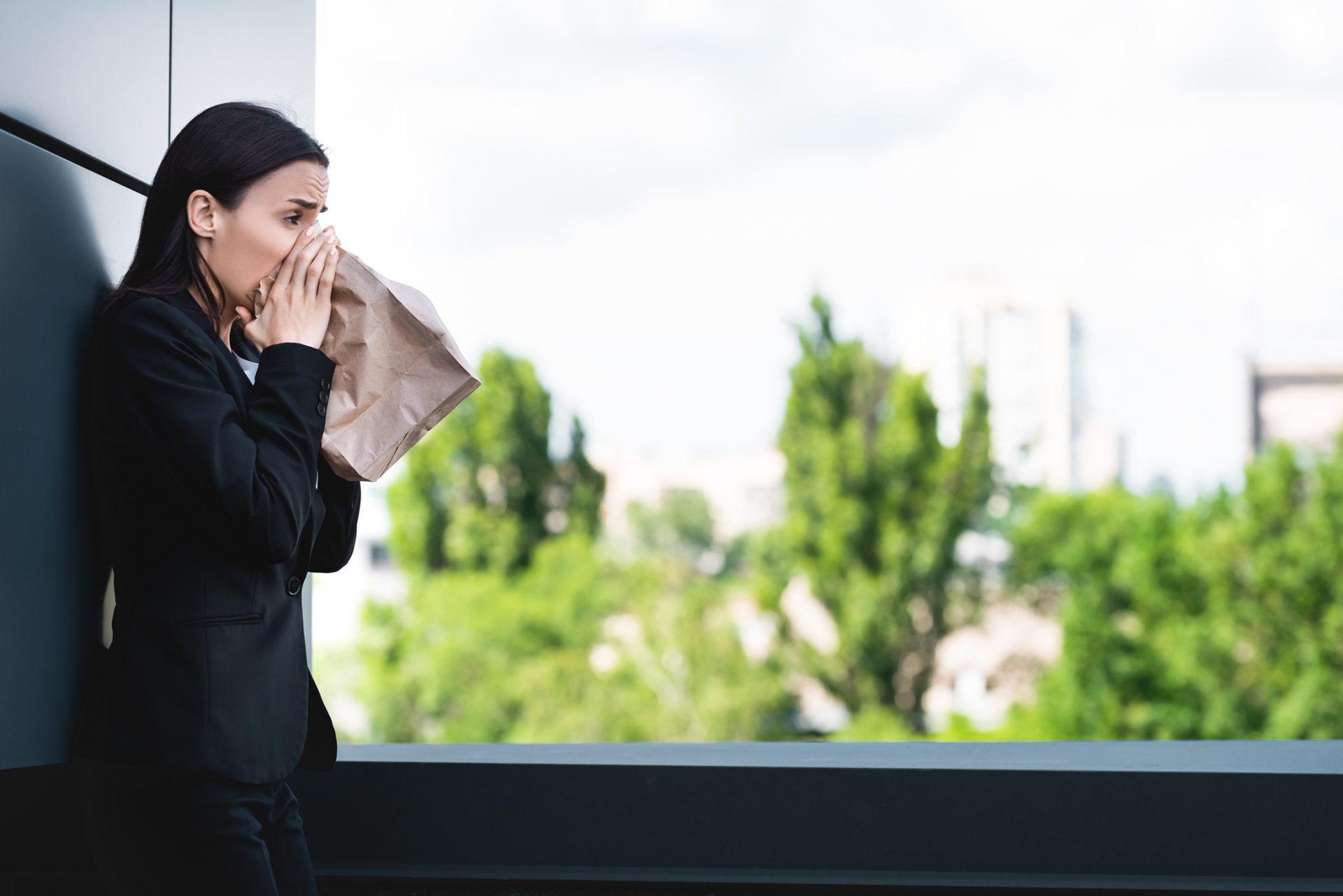 young-businesswoman-standing-on-rooftop-and-breath-2024-11-19-14-44-59-utc An attractive young businesswoman is on a roof breathing into a paper bag and appearing to panic.