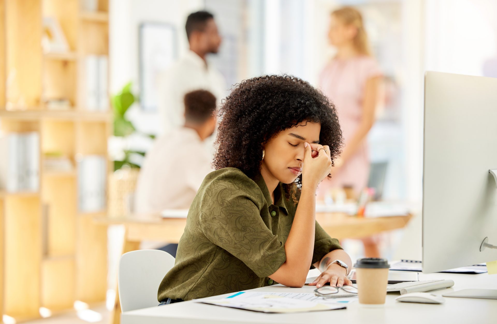 work-headache-burnout-stress-and-digital-business-2025-04-06-11-49-10-utc a young woman appears to be stressed at her desk, punching her nose with her fingers as though she has a headache.