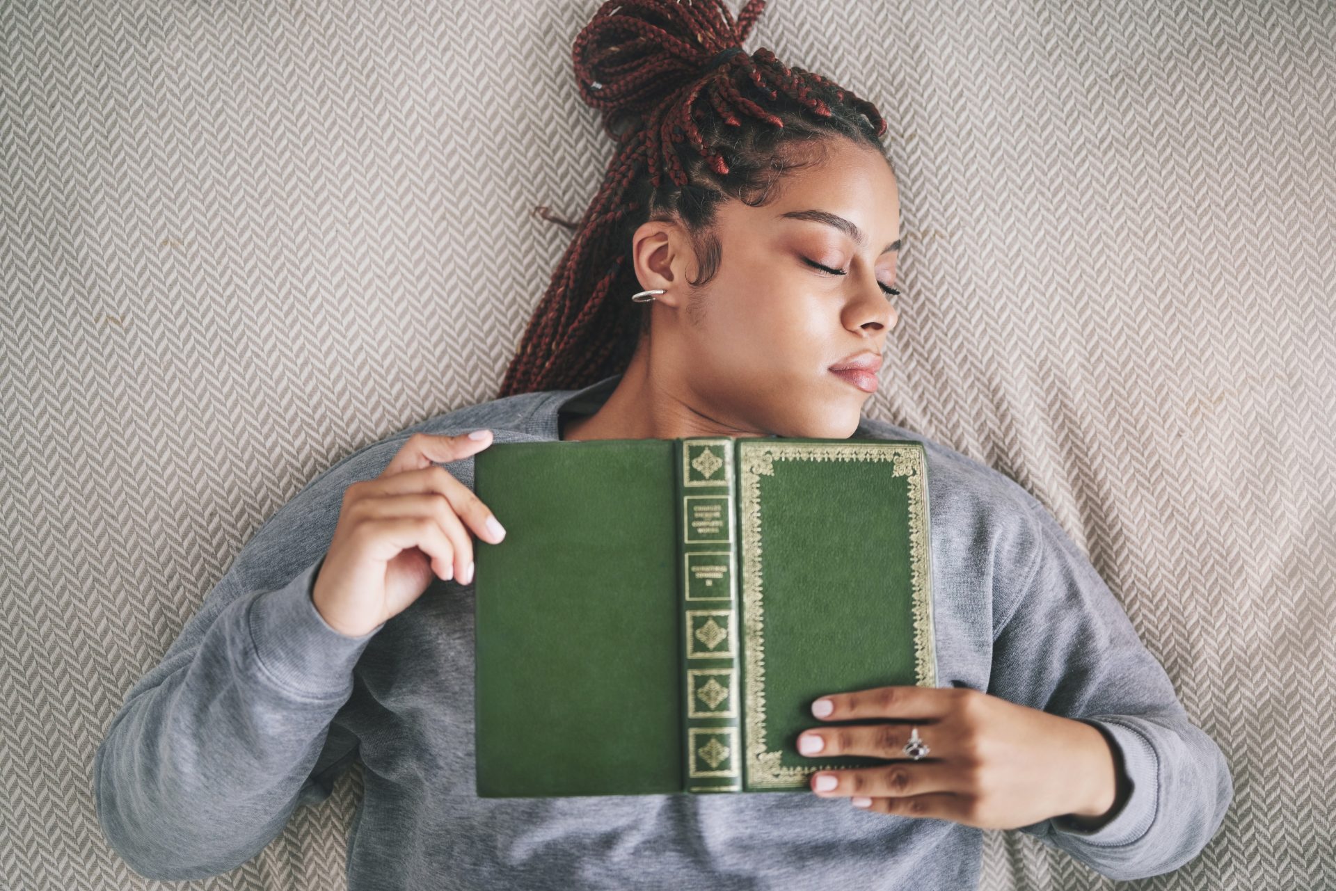 a young student with died red hair is sleeping with a green book against her chest.