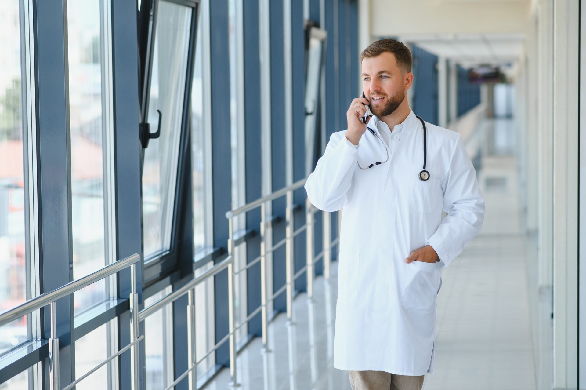 a young doctor with a beard is on a phone. his left hand is in his pocket.
