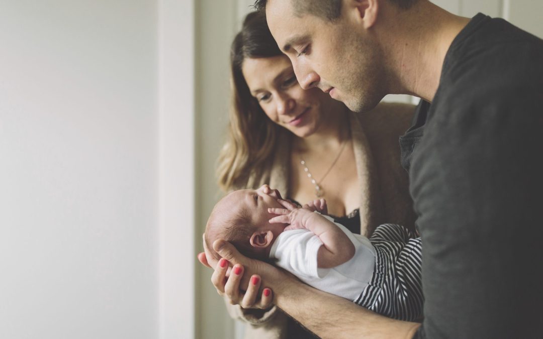 a man and a woman are looking down at a newborn baby that is crying. the baby is wearing white and black striped pants.