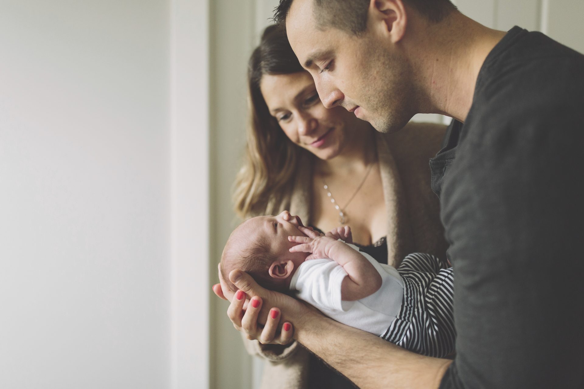 new-parents-admiring-new-born-baby-boy-2025-04-04-11-31-05-utc a man and a woman are looking down at a newborn baby that is crying. the baby is wearing white and black striped pants.