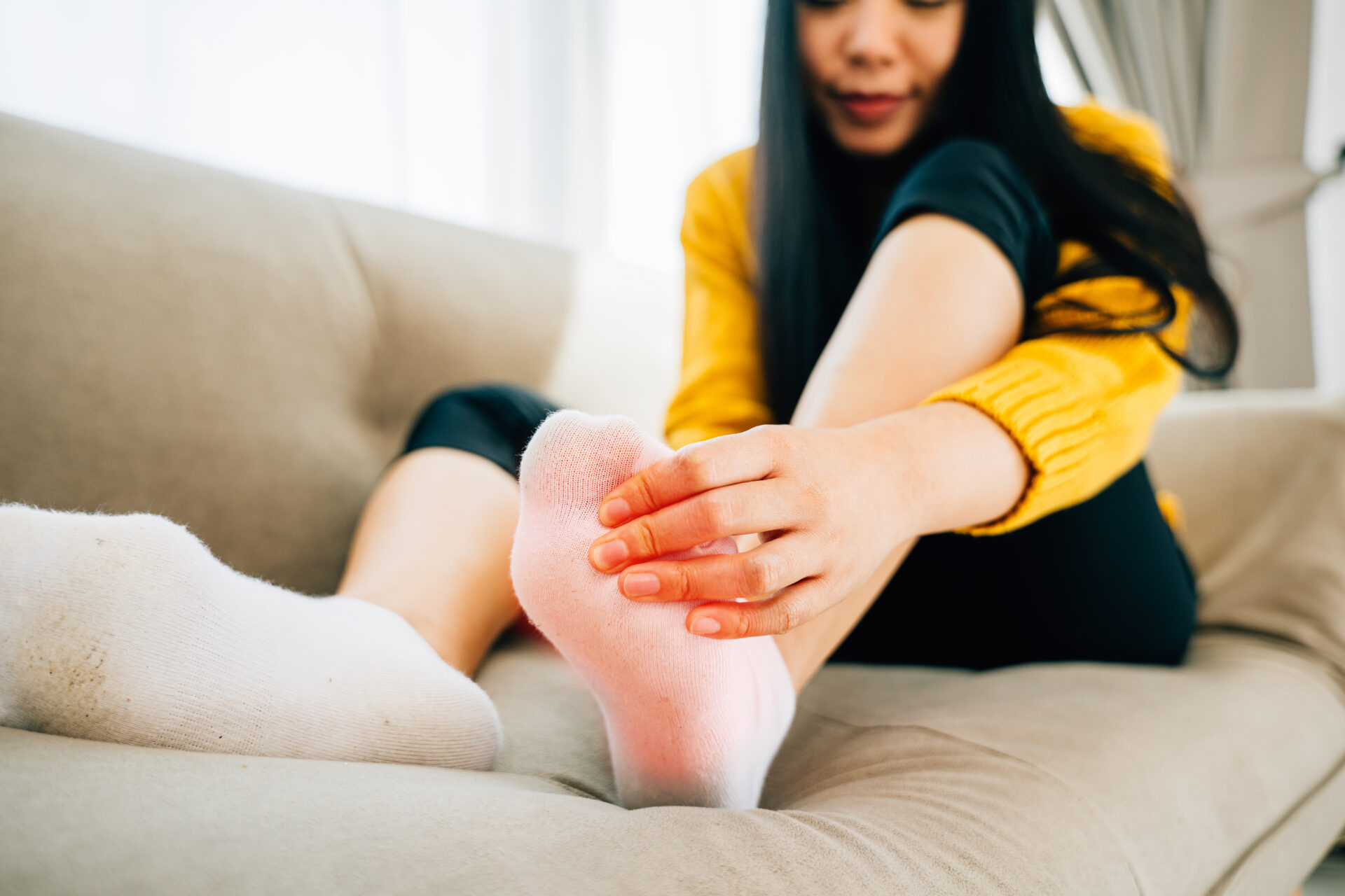A woman on a sofa massages her painful foot emphasizing the high