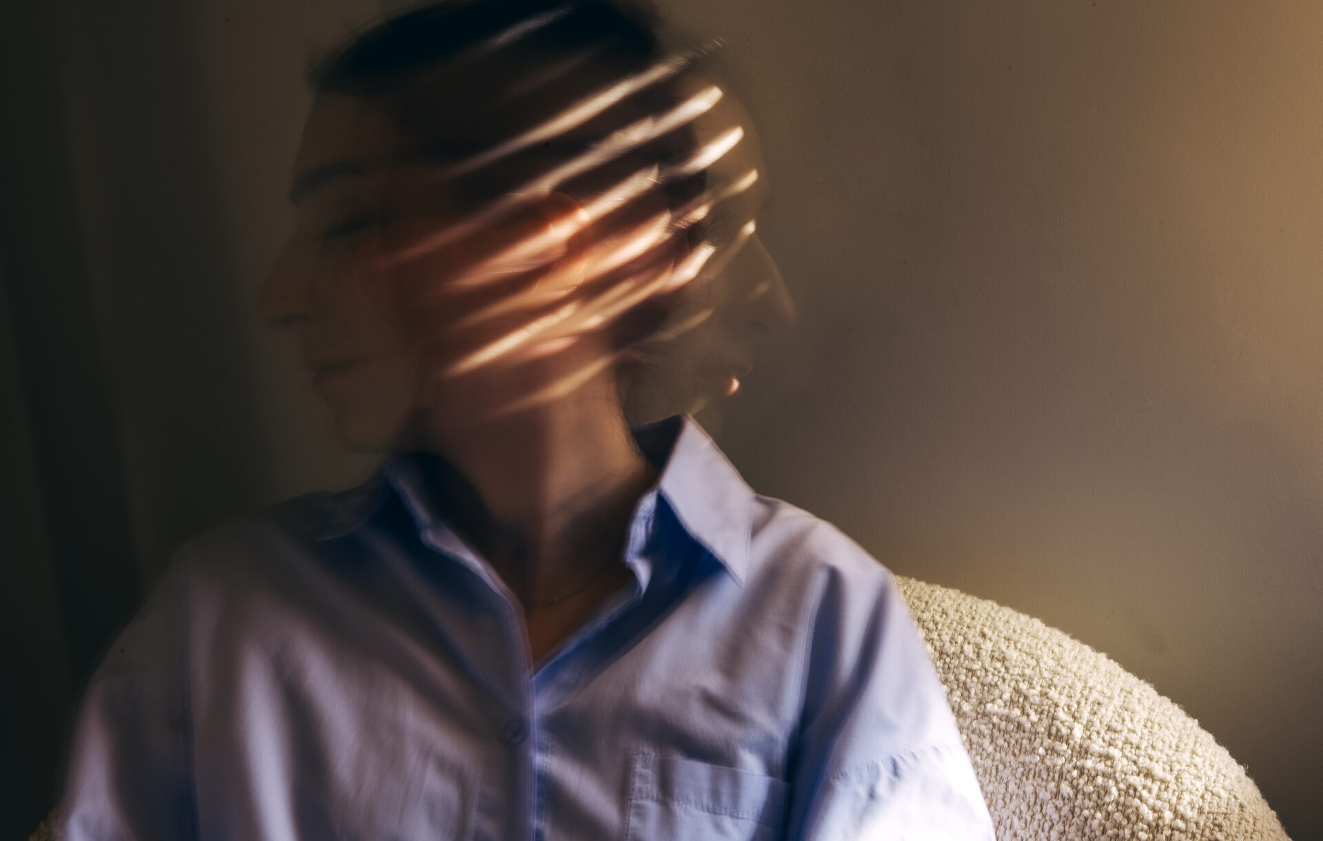 Close-up portrait of a young woman in casual clothes taken at long exposure. Blurred movements of the head of a girl in a blue shirt sitting in an armchair.